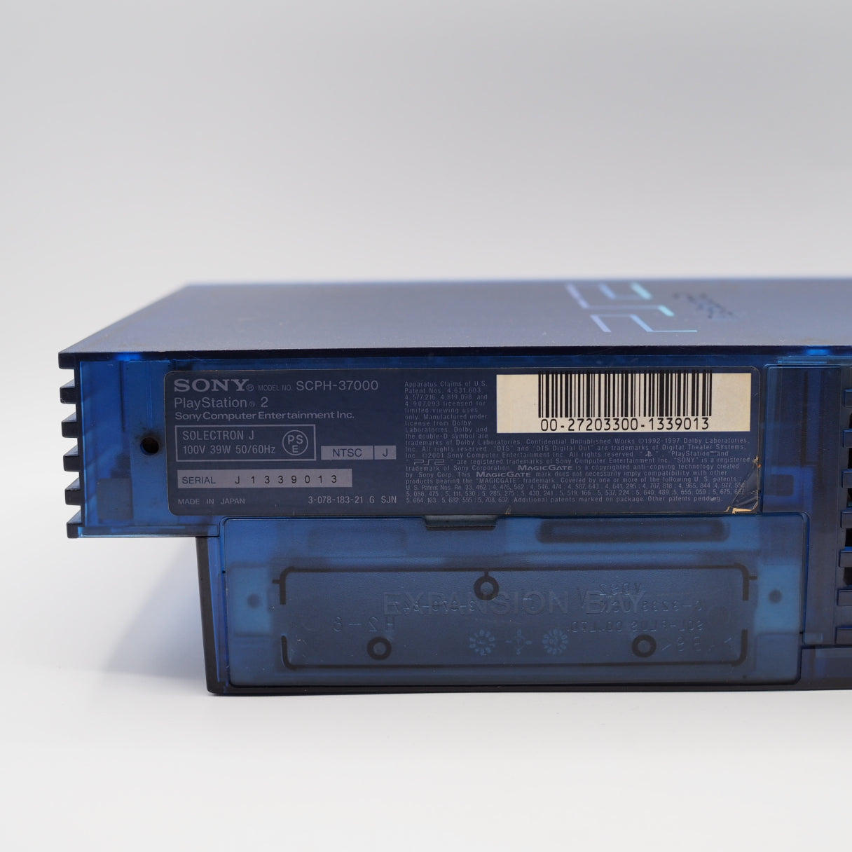 Detail of a transparent blue PlayStation 2 SCPH-37000 underside with Sony branding, serial code, and expansion bay visible.