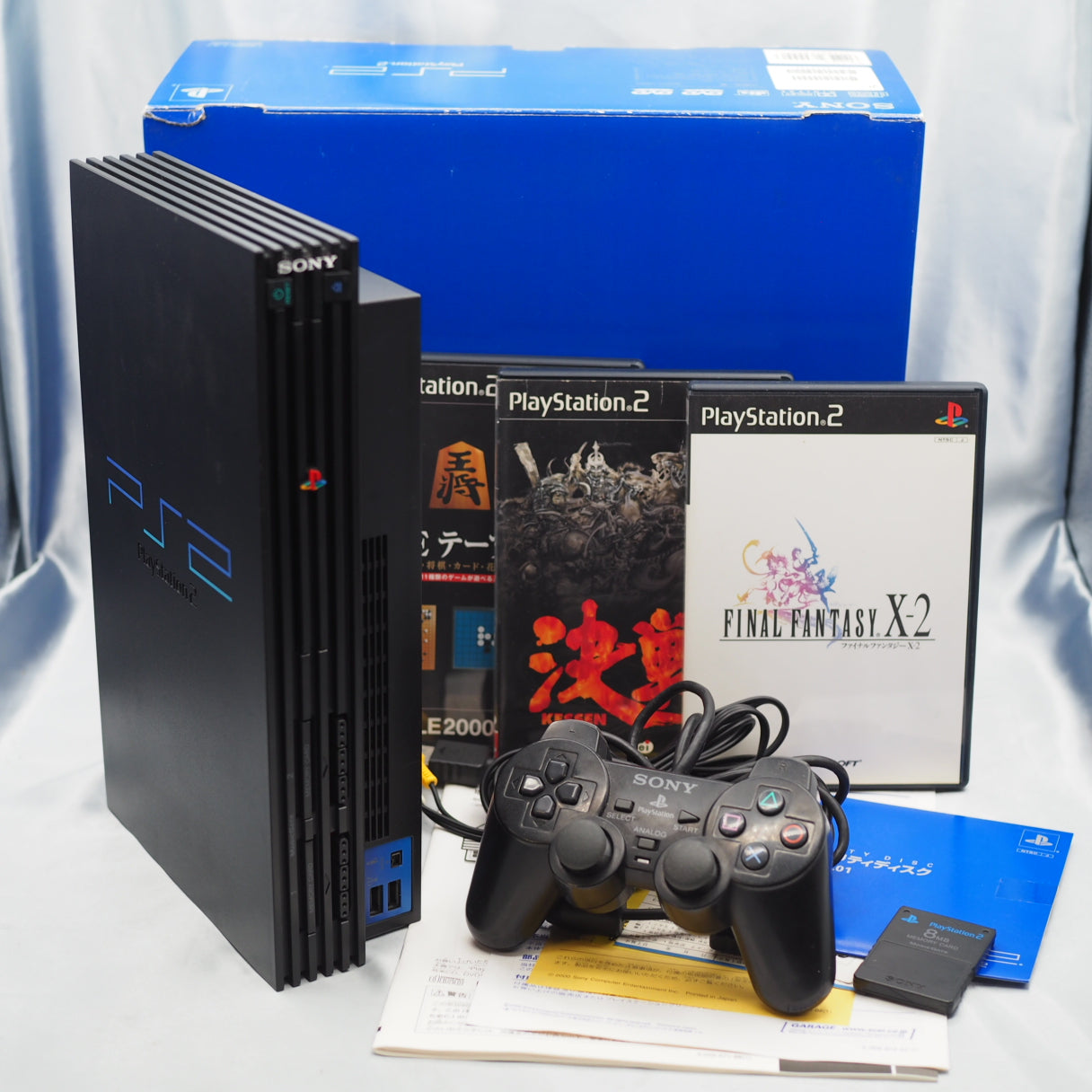 PlayStation 2 console with games, buy memory card, and controllers