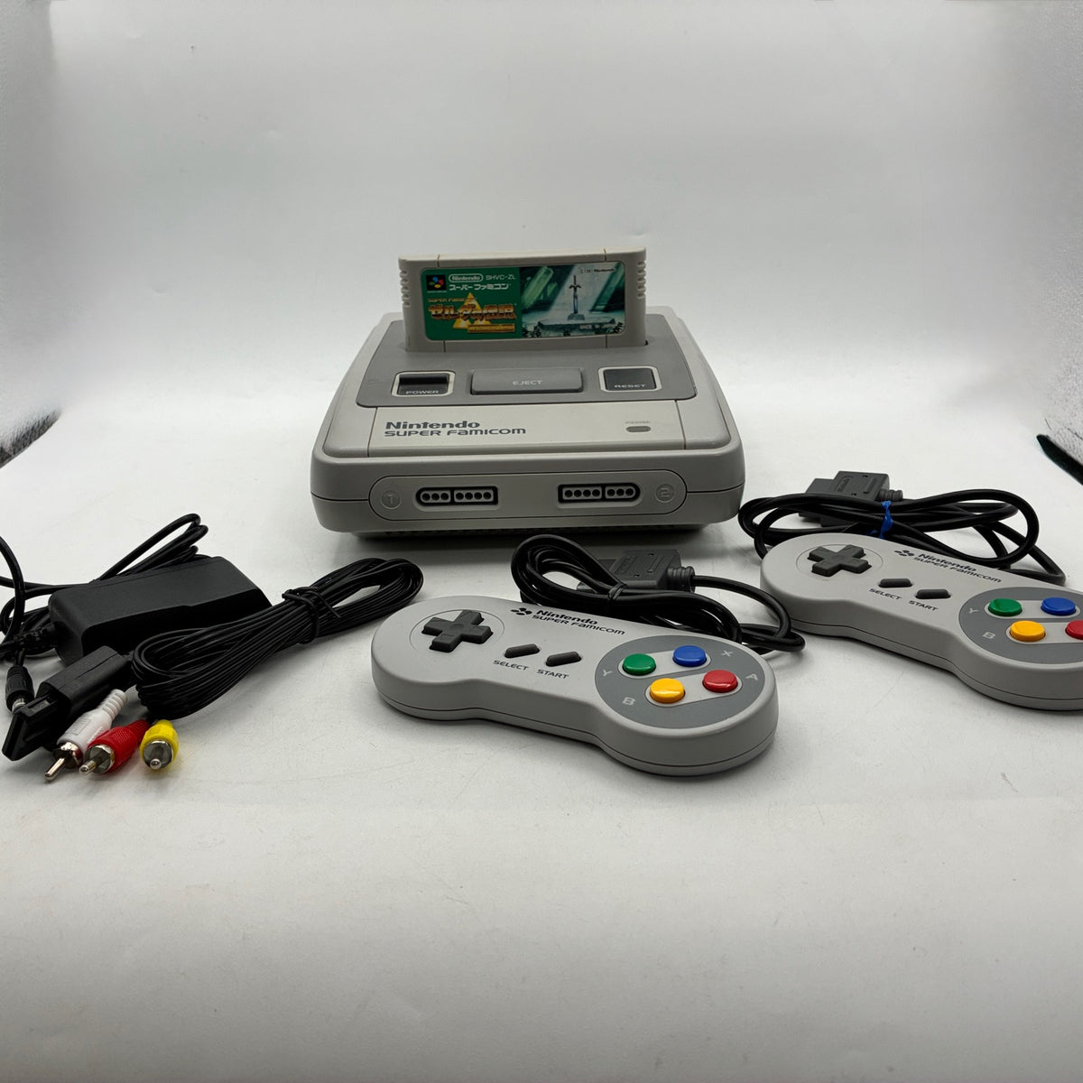 Super Famicom with The Legend of Zelda: A Link to the Past inserted, 2 controllers, AC adapter and AV cable (side view)